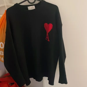 Svart stickad tröja från Ami med rött hjärta - Säljer en svart stickad tröja från Ami med ett stort rött hjärta  på bröstet. Tröjan har rund halsringning och långa ärmar. Perfekt för dig som gillar stilrena plagg med en twist.