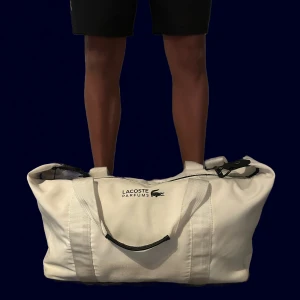 Lacoste väska - Säljer en skit snygg Lacoste väska, perfekt för sommarn när man ska till antingen skolan,jobb,stranden,gym vad som helst! Den har en liten defekt på handtaget men inget stort!