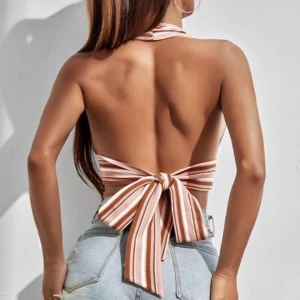 Randig halterneck topp med rosett - Säljer en croppad halterneck topp med breda beige och vita ränder. Toppen knyts i nacken och har en stor rosett i ryggen. Perfekt för sommardagar och har en öppen rygg för en luftig känsla. Det går även att knyta den på olika sätt, som att till exempel ha toppen korsad istället! (Aldrig använd)