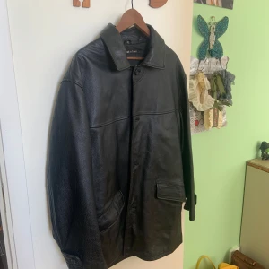 Svart skinnjacka från Best in Town - Klassisk svart skinnjacka från Best in Town i storlek XL. Jackan har lång ärm, knäppning framtill med knappar och två stora fickor. Stilren design med mjukt skinn och enkel krage.