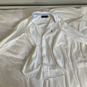 Vit skjorta från Polo Ralph Lauren (Heidi Oxford Mesh Shirt) - Vit skjorta från Polo Ralph Lauren med klassisk krage och blåvitrandiga detaljer på insidan av krage och manschetter. Broderad logga på bröstet. Perfekt för en stilren look. Nypris 1185 kr