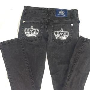 Svarta jeansbyxor med kronbroderi från Victoria Couture - Svarta jeansbyxor från Victoria Beckham/ eller couture,  med snygga vita kronbroderier på bakfickorna och lågmidjade . Klassisk femficksmodell med silverfärgade nitar och knapp. Perfekta för dig som vill sticka ut med en unik detalj på jeansen.💞💞SKAVANKER FINNS, kom privat.