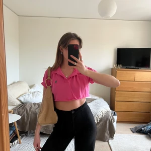 Rosa croppad polotopp från Ralph Lauren - Säljer en snygg rosa croppad polotopp från Ralph Lauren. Toppen har en klassisk krage och korta ärmar, perfekt för en trendig look. Den är dekorerad med den ikoniska Ralph Lauren-loggan på bröstet.