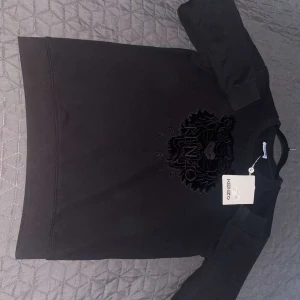 Svart tröja från Kenzo - Säljer en svart tröja från Kenzo med ett broderat tigerhuvud på framsidan. Tröjan har långa ärmar och en klassisk passform. Perfekt för en stilren look.