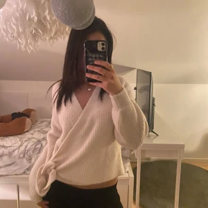 Vit omlottstickad tröja (INTE FRI FRAKT) - Säljer en mysig vit omlottstickad tröja med långa ärmar. Har en stilren design med knytning i sidan. (INTE FRI FRAKT)