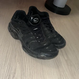 Svarta Nike tns - Säljer ett par svarta Nike tns. Skorna har en sportig design med synliga Nike-loggor och en robust sula. Perfekta för en casual look.