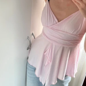 Ljusrosa topp från H&M - Säljer en söt ljusrosa topp från H&M.Denhar smala axelband och en omlott-design framtill. Perfekt för varma dagar med sin lätta och luftiga stil. Tar emot prisförslag💗