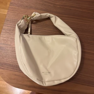 Beige axelväska från Art Street - Säljer en stilren beige axelväska från Art Street. Väskan har en knuten axelrem och en dragkedja. Aldrig använd så inga skador. Från Ullared