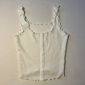 Vit ribbad linnetopp med knappar - Hej, säljer detta snygga vita ribbade linnetoppen med knappar framtill. Som även har en stilren design med volangdetaljer vid axlarna och en fyrkantig halsringning. Perfekt nu till sommaren! 