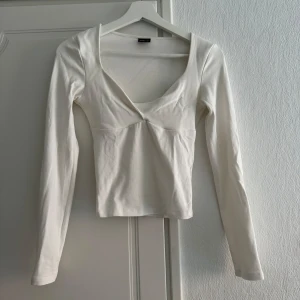 Vit långärmad topp från Gina Tricot - Säljer en stilren vit långärmad topp från Gina Tricot. Toppen har en v-ringad design och är tillverkad i ett mjukt material som ger en bekväm passform. Perfekt för en enkel och elegant look.