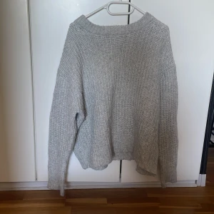 Grå stickad tröja - Mysig grå stickad tröja perfekt för kyliga dagar. Tröjan har en avslappnad passform med långa ärmar och en rund halsringning. Den är enkel och stilren, vilket gör den lätt att matcha med olika outfits.