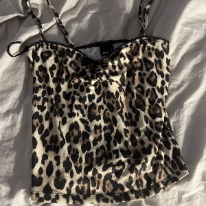 Leopardmönstrad linnetopp - Snygg leopardmönstrad linnetopp med smala axelband och dekorativ spetskant. Perfekt för en trendig look.
