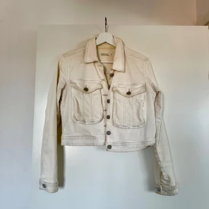 Vit/Beige jeansjacka  - En fin gräddvit/beigeaktig jeansjacka från Unique You. Den har en croppad design med knappar framtill och två stora fickor med lock på bröstet. Superfin nu till våren 🌸