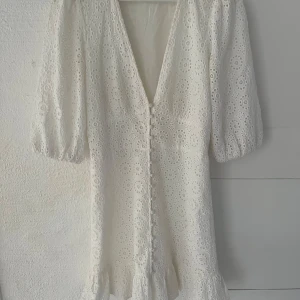 Vit klänning från Gina Tricot - Charmig vit klänning  från Gina Tricot med v-ringning och knappar framtill. Klänningen har puffiga trekvartsärmar och volangdetaljer vid fållen. Perfekt för sommarens festligheter eller student! Jöttebraskick! Storlek m men passar en s. Pris går att diskutera 