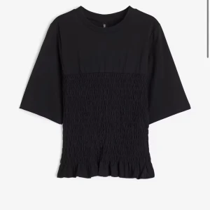 Svart topp med smockdetaljer - Snygg svart topp med smockdetaljer och volangkant. Toppen har trekvartsärmar och passar till det mesta 