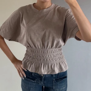 Beige kortärmad topp med resårdetalj - Säljer en beige kortärmad topp med resår i midjan som ger en fin volangeffekt. Från hm❤️