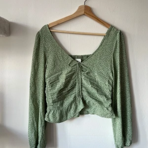 Grön blommig blus från H&M - Säljer en söt grön blommig blus från H&M med långa ärmar och en knytning framtill. Perfekt för vår och sommar!