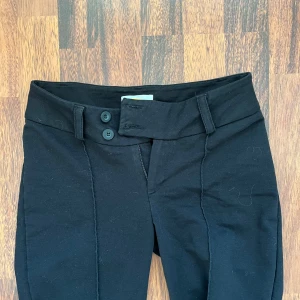 Svarta byxor från Gina Tricot - Snygga svarta byxor från Gina Tricot med låg midja och bootcut-stil. Byxorna har en stilren design med knappar framtill och är perfekta för en chic look. Ej använda och priset kan diskuteras 