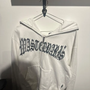 Vit hoodie med tryck från Masterworks - Säljer en vit hoodie från Masterworks med ett coolt tryck av en spindel på baksidan och text på framsidan. Hoodien har dragkedja och en stor ficka framtill. Perfekt för en avslappnad stil.