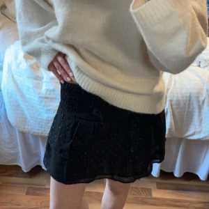 Svart kortkjol med glitter - Snygg svart kortkjol med glittrigt mönster. Kjolen har en elastisk midja för bekväm passform och en lätt volangdetalj vid fållen. Perfekt för att lägga till lite glitter i din outfit!