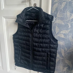 Svart dunväst från Lindex - Snygg svart dunväst från Everest med dragkedja framtill. Perfekt för lager-på-lager under kyliga dagar. Västen har en stilren design med quiltade detaljer och hög krage. Priset går att diskutera!