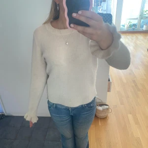 Vit stickad tröja - Säljer en mysig vit stickad tröja med rund hals och långa ärmar. Perfekt för kyligare dagar och lätt att matcha med jeans eller kjol. Tröjan har en klassisk design med ribbade muddar vid ärmslut och nederkant.