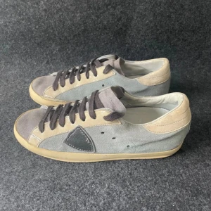 Grå sneakers från Philippe Model - Snygga grå sneakers från Philippe Model med beige och svarta detaljer. Perfekta för en stilren vardagslook.