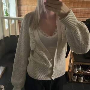 Vit stickad kofta från Holly & Whyte Storlek S - Superfin vit stickad kofta från Holly & Whyte med dekorativa guldknappar och vackert hålmönster. Koftan har långa ärmar och ribbade muddar. Perfekt att slänga över en topp för en mysig look.