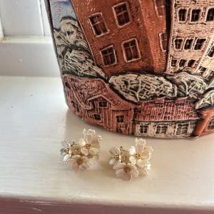 Blommiga örhängen i vitt och guld - Säljer superfina örhängen med vita blommor och små pärldetaljer. Blommorna har guldfärgade detaljer i mitten och örhängena är i en klusterdesign som ger ett unikt och elegant intryck. Nyskick, endast använt vid 1 tillfälle och nu när jag tog bilden!🥰