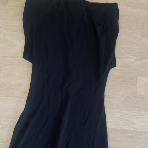 Svart långklänning - En stilren svart långklänning med figurnära passform. Klänningen har en enkel design utan synliga detaljer eller mönster, vilket gör den lätt att styla. Perfekt för dig som gillar minimalistiskt mode.