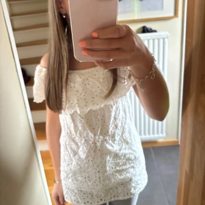 Vit offshoulder blus från D-XEL - Säljer en söt vit offshoulder blus från D-XEL med broderade detaljer och volang upptill. Blusen har resår vid axlarna. Perfekt för varma dagar! Lite längre i modellen men man kan sy upp eller vika. Priset är diskuterbart! Läs bio💘