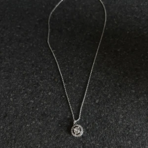 Lily and Rose halsband  - Ett elegant halsband i silverfärg med en tunn kedja och en rund, glittrig berlock dekorerad med små stenar. Aldrig använd. 