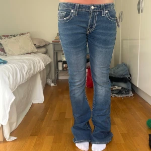 Blå bootcut jeans från true religion - Snygga blå jeans med bootcut passform och tydliga vita kontrastsömmar. Klassisk femficksmodell med låg midja och dekorativa bakfickor. 