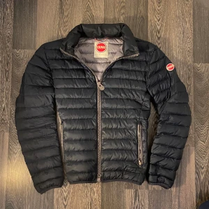 mörkblå pufferjacka från Colmar - Säljer en mörkblå pufferjacka från Colmar med klassisk logotyp på ärmen. Jackan har dragkedja framtill och två sidofickor med dragkedja. Perfekt för kyligare dagar och har en stilren, sportig look.