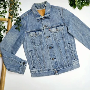Klassisk jeansjacka från Levi's - Klassisk blå truckerjacka från Levis. Jackan är i storlek xs men modellen är stor så passar också som s. Jackan har knappar framtill, två bröstfickor med lock och knapp samt två sidofickor. Knappt använt och är i fint skick.   Mått:  Längd från axel och neråt: 61 cm Längd från armhåla och ner: 46 cm  Ärmlängd: 62 cm
