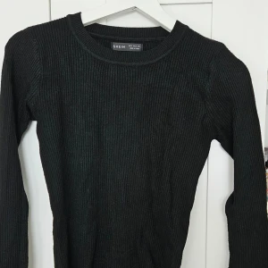 Svart ribbad långärmad tröja från SHEIN - Säljer en svart ribbad långärmad tröja från SHEIN. Tröjan har rund halsringning och är figurnära i modellen. Perfekt att matcha med jeans eller kjol för en enkel och stilren look.