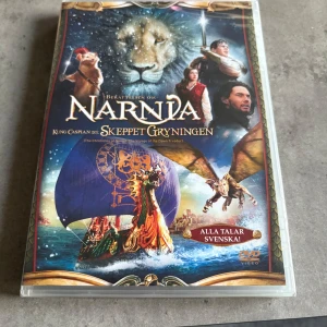Berättelsen om Narnia: Skeppet Gryningen - DVD-film med äventyr och fantasytema, baserad på C.S. Lewis bokserie om Narnia. Omslaget visar ett skepp, en lejon och flera karaktärer från filmen. Filmen är på svenska och har färgstark framsida med magiska inslag. Inplastad 