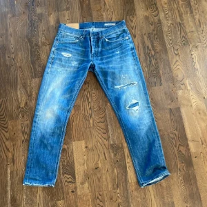 Dondup George  - Säljer ett par blå jeansbyxor med slitningar och hål på benen. Klassisk femficksmodell med normal passform och raka ben. Perfekta för en avslappnad och trendig look. Storlek 32 men passar även mindre 