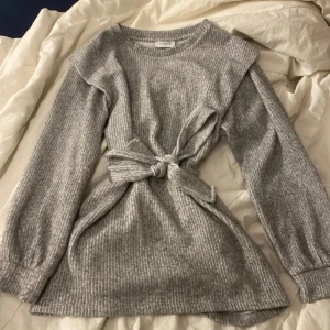 Grå ribbad stickad tröja med knyt från Papaya - Supermjuk grå stickad tröja från Papaya med ribbad struktur och knytband i midjan. Långärmad modell med rund halsringning, perfekt för lager-på-lager och chill dagar.