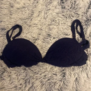 Mörkblå vadderad bikiniöverdel - Säljer en mörkblå bikiniöverdel med vadderade kupor och dubbla axelband. Toppen har ett diskret mönster i tyget och justerbara band för bästa passform. Perfekt för stranden eller poolen!