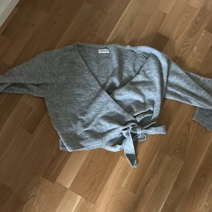 Grå omlottopp från Even&Odd - Säljer en grå omlottopp från Even&Odd med knyt i midjan. Tröjan har lång ärm och är tillverkad i ett mjukt stickat material. Perfekt för lager-på-lager och enkel att styla till olika outfits.