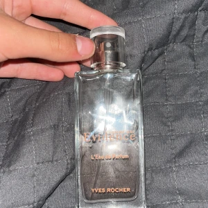 Parfym 'Comme une Evidence' från Yves Rocher - Säljer en elegant parfymflaska 'Comme une Evidence' från Yves Rocher. Flaskan är rektangulär i genomskinligt glas med silvrig spraykork och text i guld. Doften är en klassiker från märket och passar dig som gillar fräscha och blommiga toner.