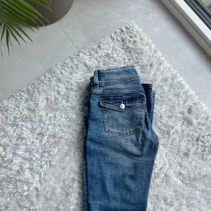 Blå bootcut jeans från Gina Tricot - Snygga blå bootcut jeans från Gina Tricot med klassisk femficksdesign och dubbla knappar i midjan. Jeansen har en lätt tvättad look och är perfekta för dig som gillar en tidlös stil. Byxorna har använts men inte fått några skador eller någon sömm som har gått upp!