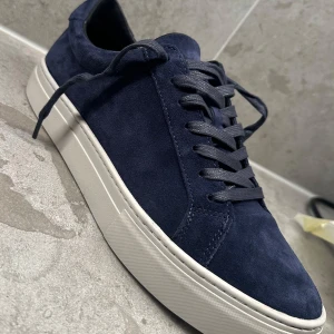 Mörkblå sneakers från Vagabond - Snygga mörkblå sneakers från Vagabond i mocka med vita platta sulor. Skorna har rund tå och klassisk snörning. Perfekta för dig som gillar stilrena och tidlösa skor. Modell: Vagabond Paul 2.0, testade endast en gång, nypris 1400 kr. Har gått mer än 14 dagar så kan inte lämna tillbaka.