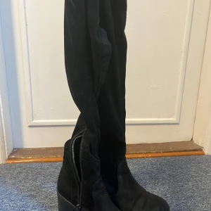 Svarta lårhöga stövlar med klack - Säljer ett par svarta lårhöga stövlar med klack och dragkedja på insidan. Skorna har en rund tå och är tillverkade i mocka-liknande material. Perfekta för att lyfta vilken outfit som helst. Skriv om fler bilder behövs! 🌸