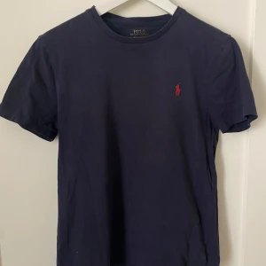 Mörkblå t-shirt från Polo Ralph Lauren - Säljer en mörkblå T-shirt från Ralph lauren i storlek S. Tröjan är i perfekt skick förutom lite slitning på loggan i nacken. Skriv om ni har frågor!