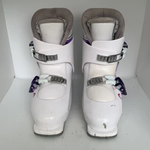 Vita pjäxor från HEAD med lila detaljer - Säljer ett par vita pjäxor från HEAD med lila och grå detaljer. Pjäxorna har två spännen i metall och plast, samt vadderad insida för extra komfort. Snygg HEAD-logga på sidan och dekorativa mönster i lila.