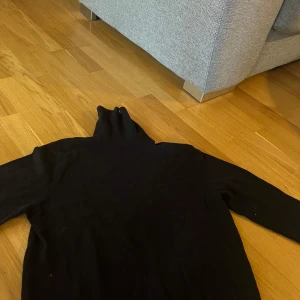 Svart polotröja från H&M - Säljer en svart polotröja från H&M i slim fit-modell. Tröjan har långa ärmar och är perfekt för lager-på-lager-stil. Enkel och stilren design som passar till många olika outfits.
