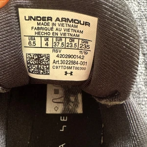Svarta sneakers från Under Armour - Säljer ett par svarta sneakers från Under Armour med vit sula och svarta snören med vita prickar. Skorna har en sportig design med mesh-överdel och logga på plösen. Perfekta för träning eller vardagsstil.