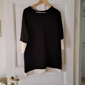 Svart och vit stickad tröja - Snygg svart stickad tröja med kontrasterande vita muddar vid ärmslut och nederkant. Modellen har trekvartsärm och rak passform, perfekt för en stilren look. Enkel att matcha med accessoarer för en personlig touch.